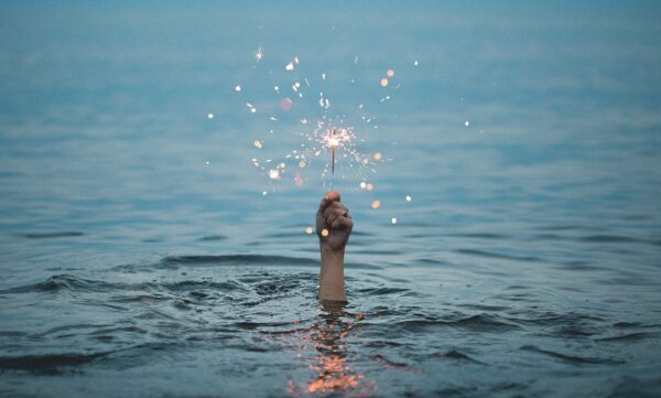 Eine Hand ragt aus dem Wasser und hält eine angezündete Wunderkerze.