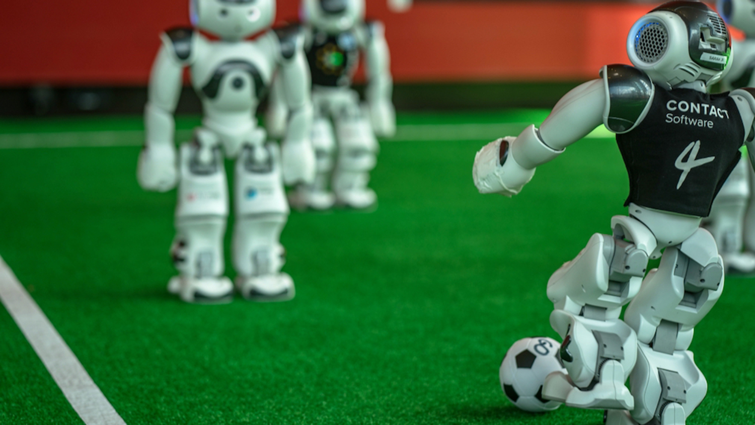 Mehrere Roboter spielen Fußball auf einem Kunstrasenfeld