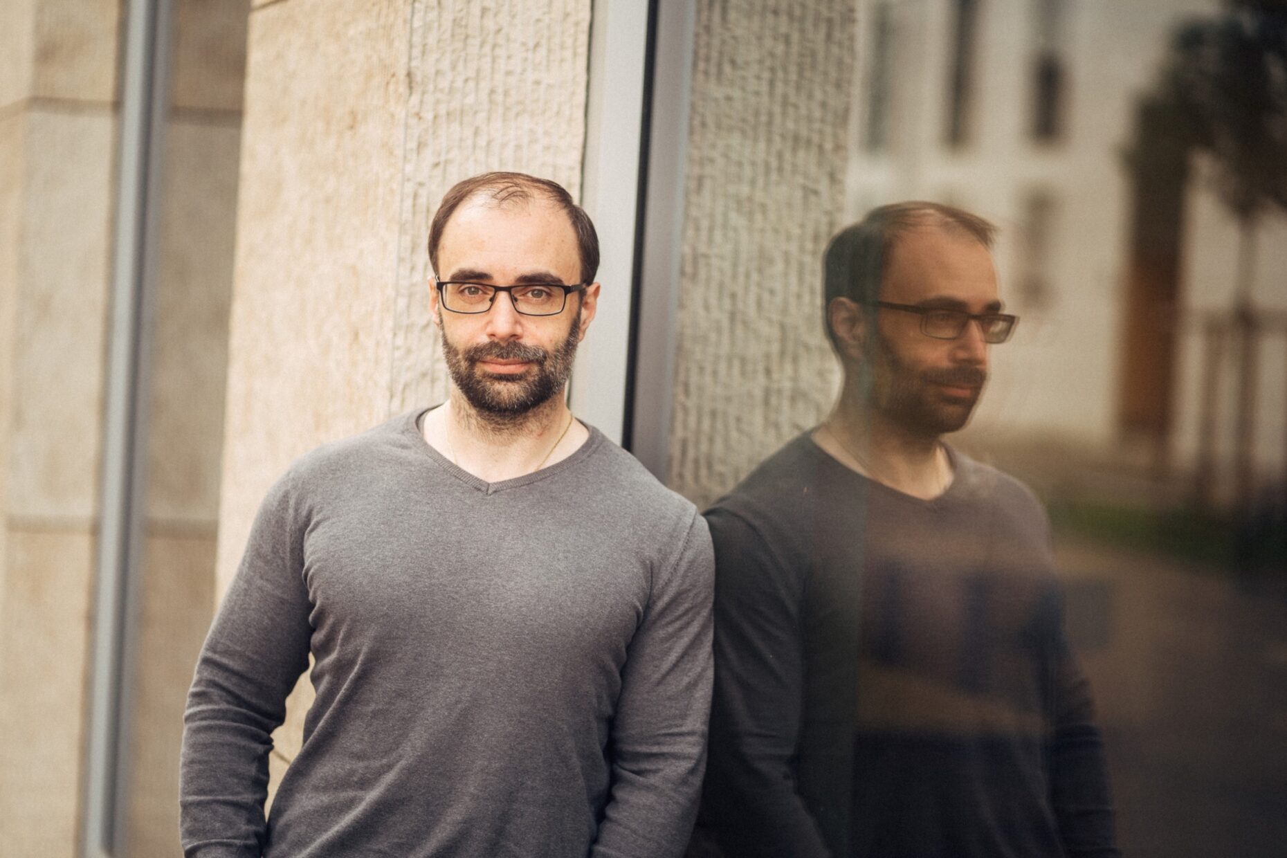 Portraitfoto eines Mannes, der an eine Glasscheibe gelehnt in die Kamera schaut.