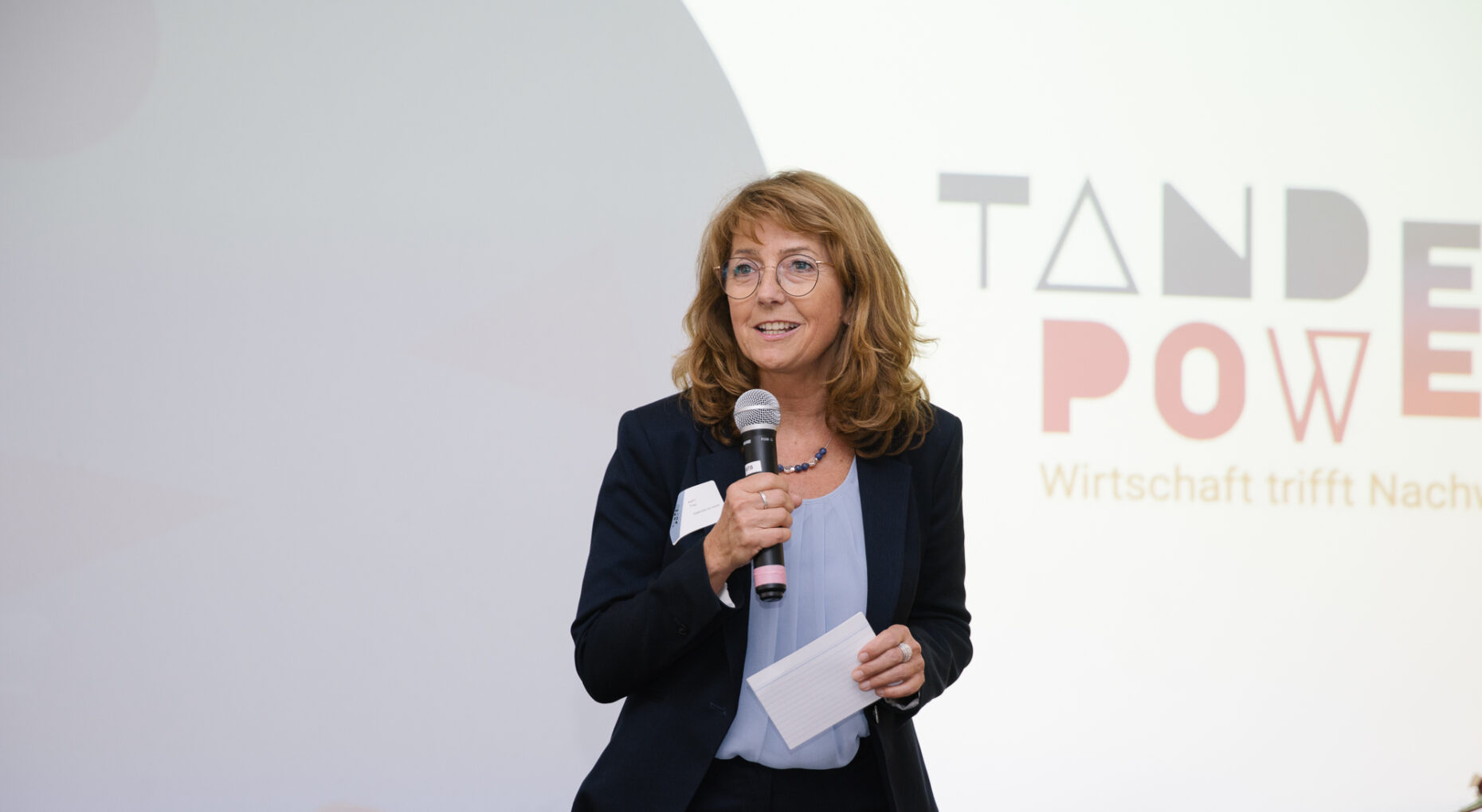 Eine Frau steht mit Mikro vor einer PowerPoint -Präsentation und spricht.