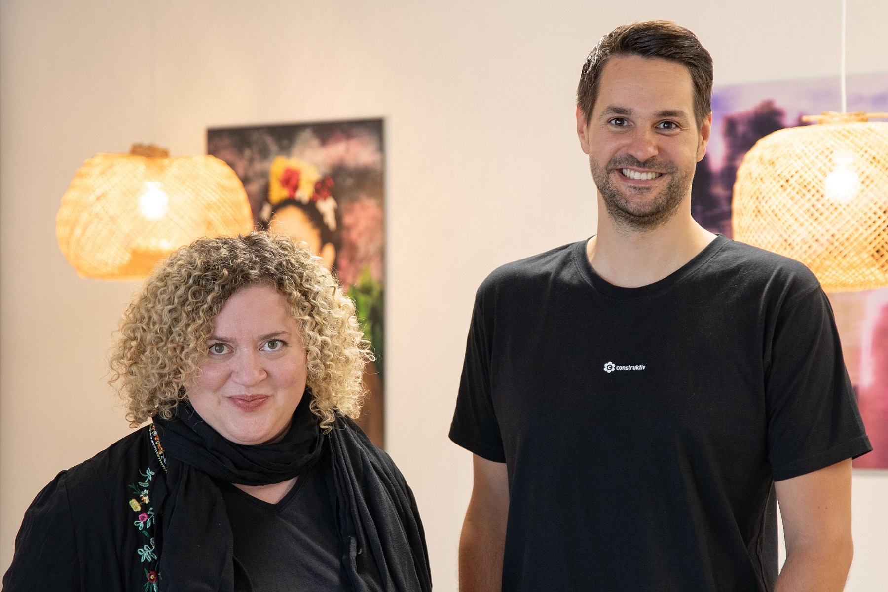 Ein Mann und eine Frau stehen nebeneinander vor einer hellen Wand und lächeln in die Kamera.