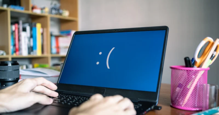 Aufgeklappter Laptop steht auf Tisch. Auf dem Bildschirm ist ein mit Doppelpunkt und offener Klammer getippter unzufriedener Smiley zu sehen.