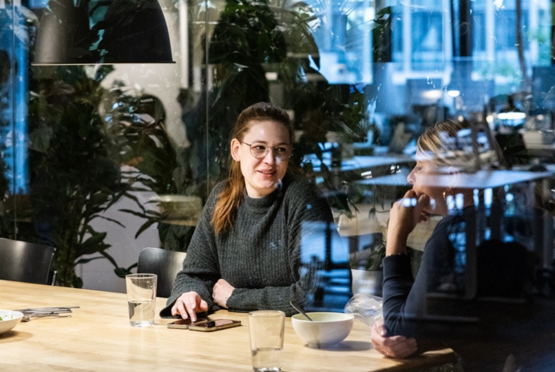 Blick duch einen Glasfront auf zwei Personen, die an einem Tisch sitzen und sich unterhalten.