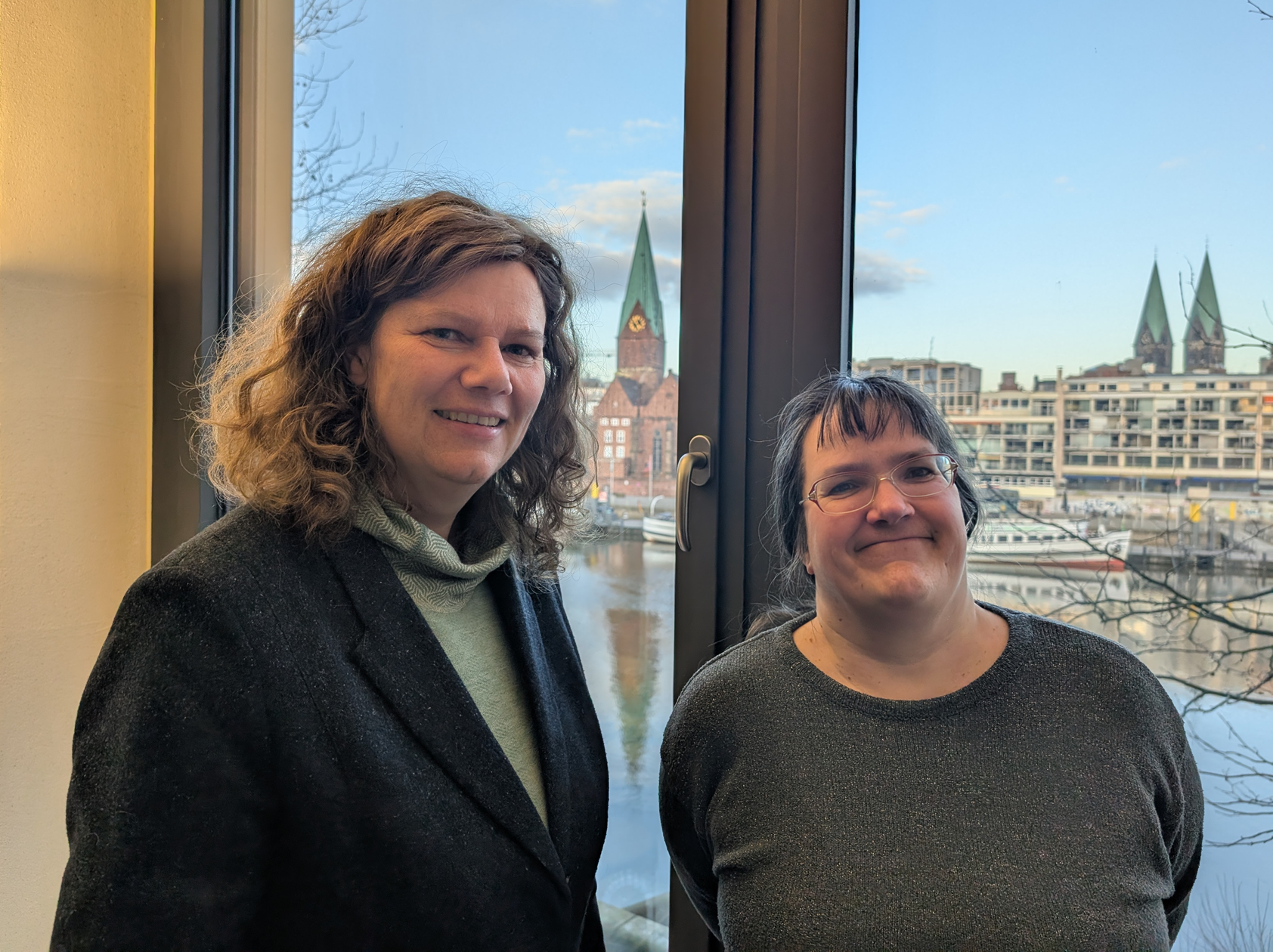 Zwei Frauen stehen auf einem Fenster und lächeln in die Kamera. Im Hintergrund ist die Weser zu sehen.